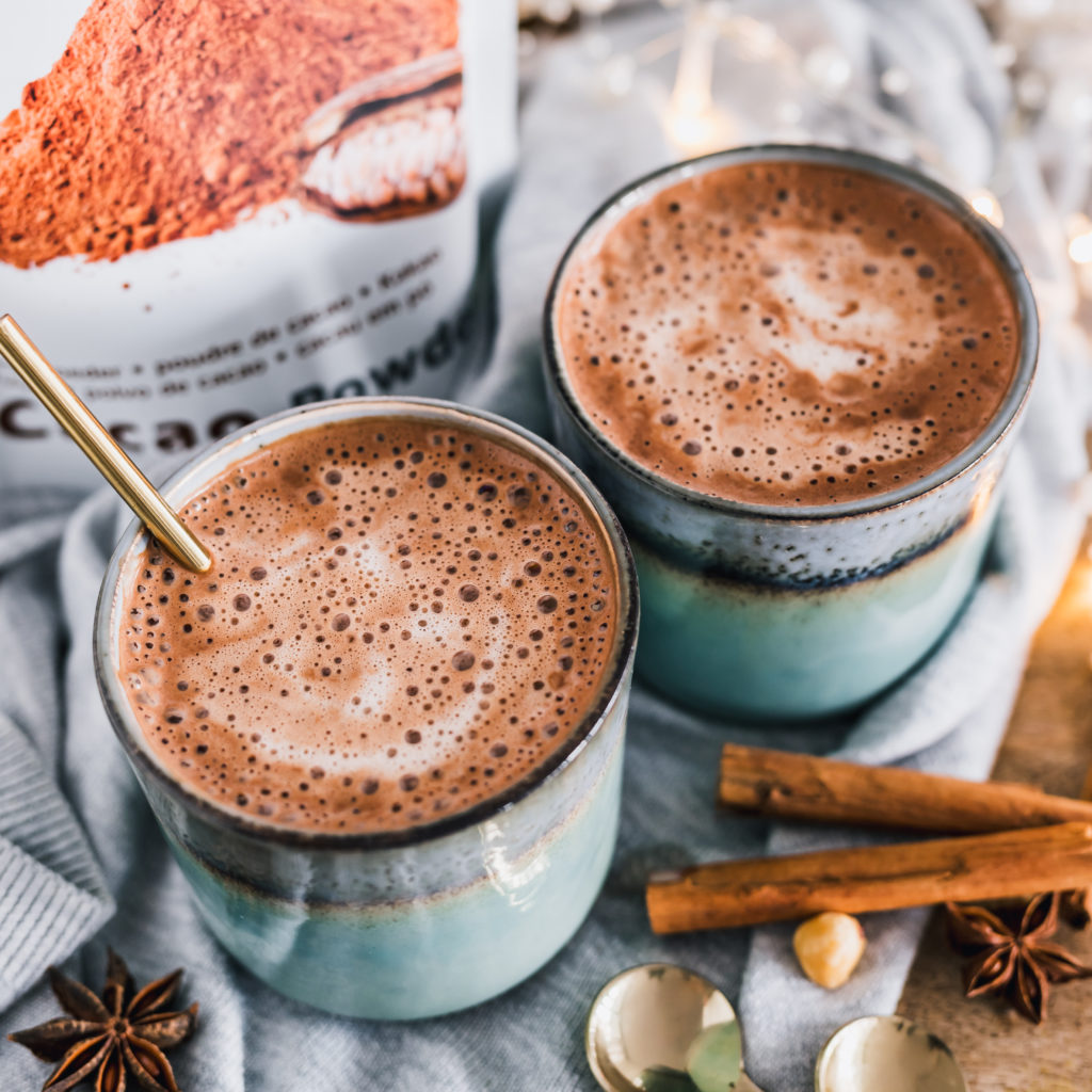 Chai latte met cacaopoeder, twee geglazuurde koppen met kaneelstokjes